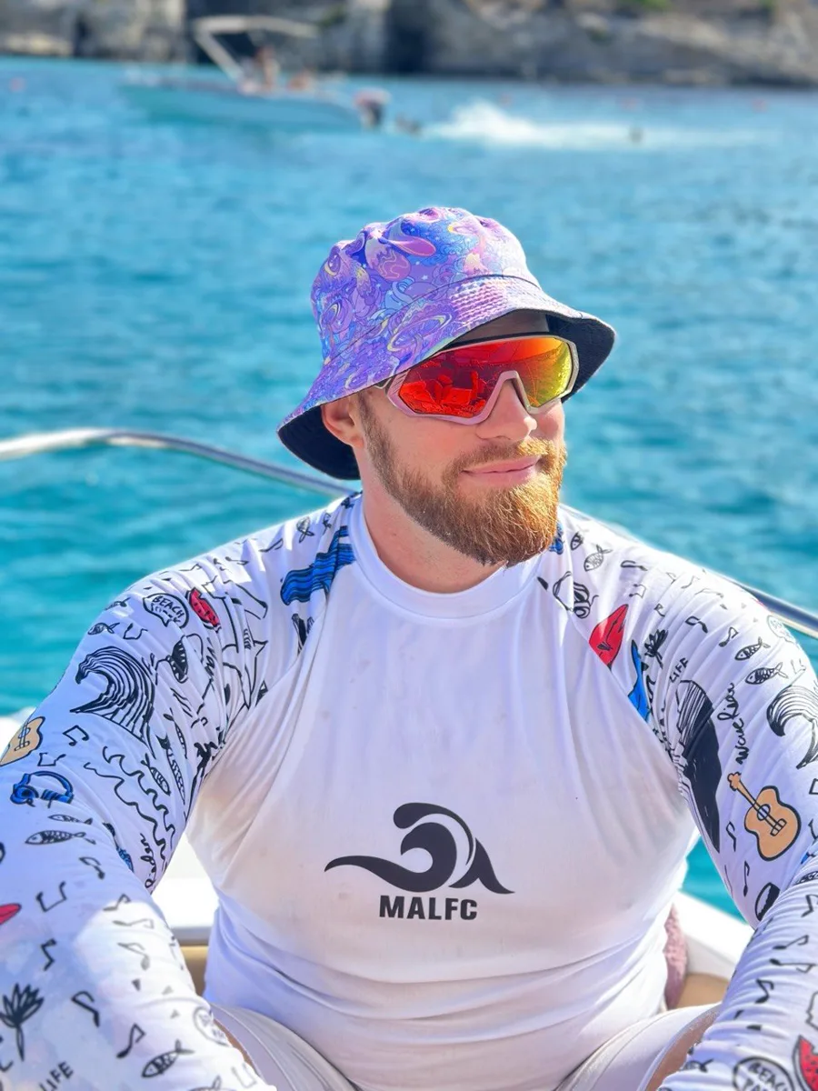 Your SUP Lovers guide in a bucket hat and sunglasses, smiling on a boat over turquoise water